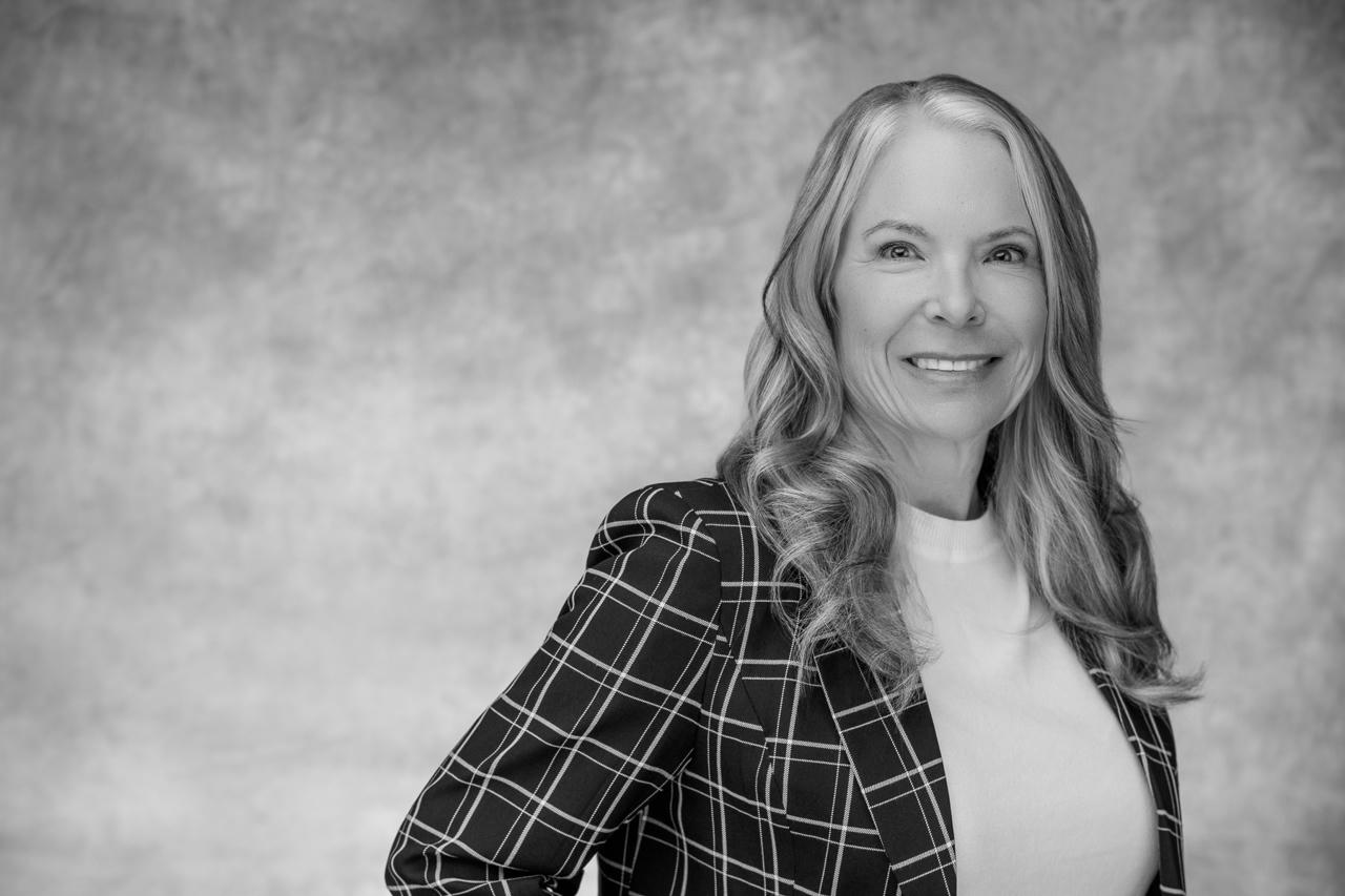 Smiling woman in checkered blazer, grayscale portrait.